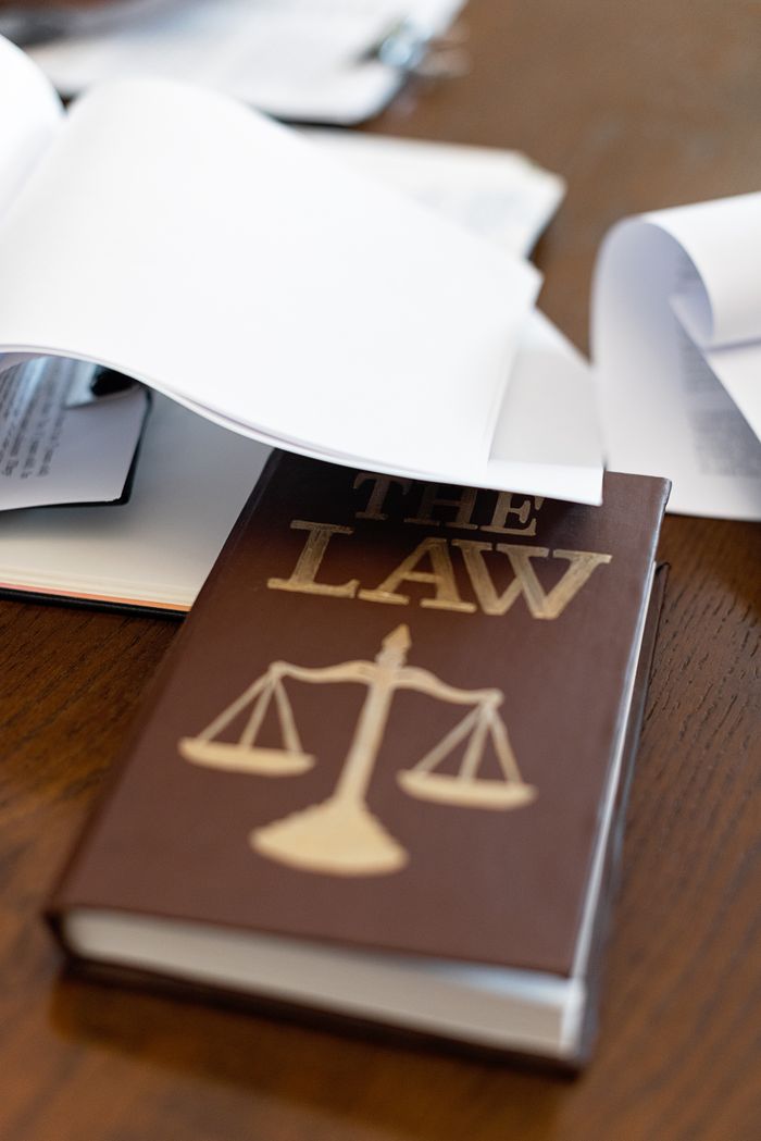 Services Close-up of a law book with scales icon on a wooden desk covered in papers.
